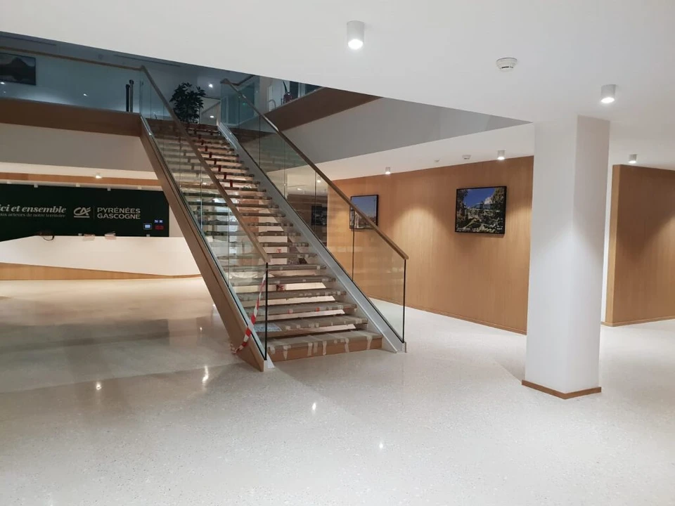 Ouvrier en tenue de travail multicolore utilisant une ponceuse à béton électrique dans un espace intérieur en construction